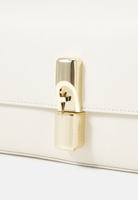 Witte leren handtas met textuur, voorzien van een glanzende goudkleurige sluiting en gedetailleerde stiksels langs de randen. Compact rechthoekige vorm.