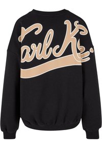 Svart hettegenser med en stor grafisk tekstdesign i beige som leser "Karl K." med en buet linje under. Ribbede mansjetter og hem.