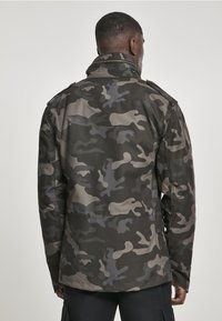 Maskáčová bunda v tmavě zelené, šedé a taupe barvě. Disponuje límečkem, knoflíkovými detaily a strukturovaným designem se zadními kapsami.