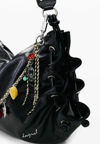 Mustast nahast kott volditud servadega, metallist detailide ja erinevate värvidega dekoratiivsete ripatsitega. Varustatud kinnitusnööriga ja logoga detailiga.