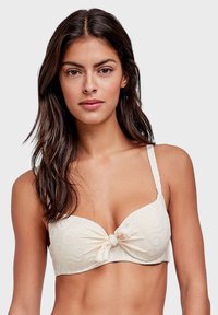 Reggiseno color crema con centro annodato, spalline regolabili e un motivo testurizzato a cerchi sul tessuto.