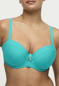 Turkusowy biustonosz z fiszbinami o prążkowanej fakturze, regulowanymi ramiączkami i złotym okrągłym akcentem na środku z przodu, o wspierającym kroju.