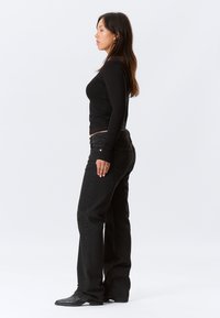 Top a maniche lunghe nera abbinato a jeans a zampa d'elefante in denim scuro. L'outfit presenta una silhouette aderente e maniche lunghe. Dettaglio distintivo dei passanti della cintura visibile.