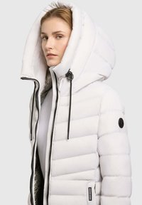 White puffer jacket with a large, adjustable hood. Features quilted design, two-way zipper, and a branded patch on the sleeve.