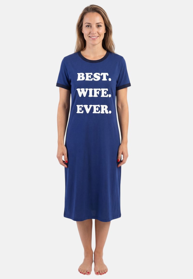 Mujer sonriente está descalza vistiendo un vestido midi azul con mangas cortas y texto blanco en el frente que dice "LA MEJOR. ESPOSA. DE TODAS."