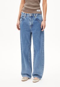 Wide-leg blue denim jeans with a light wash, featuring a button closure, five pockets, and visible stitching. Made from durable cotton fabric.