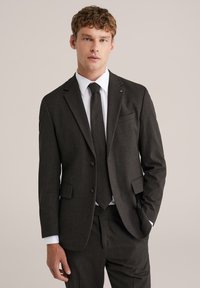 Ogļu pelēks uzvalks ar strukturētu dizainu, kuram ir žakete ar vienu pogu, ieliektu apkakli un saskanīgu kaklasaiti. Tekstūra audums un krūšu kabata.