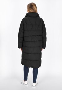 Sort pufferjakke med høj krave, lange ærmer og længde til midt på læggen. Har et quiltet design og en glat, skinnende overflade.
