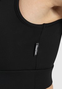 Sujetador deportivo negro con escote redondo, tejido texturizado y etiqueta con logo en el lateral. Presenta un diseño ajustado y una banda elástica en la parte inferior.