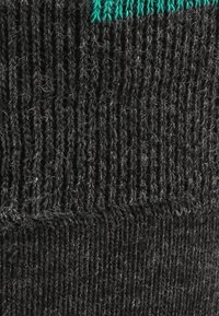 Schwarzer Strickstoff mit strukturierter Oberfläche. Verfügt über einen kontrastierenden türkisfarbenen Streifen am oberen Rand, der gerippte und glatte Abschnitte zeigt.