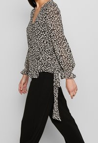 Blouse à imprimé léopard noir et blanc avec de longues manches bouffantes et un détail à nouer à la taille, fabriquée en tissu léger et transparent.
