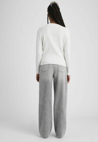 Pull blanc avec ourlet côtelé, associé à un jean gris clair taille haute et coupe évasée, doté de poches arrière et d'un délavage.