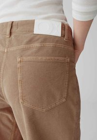 Pantalon en velours côtelé marron avec une coupe légèrement ajustée. Comprend une étiquette de marque blanche à la taille et une poche arrière avec des détails cousus.