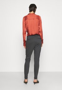 Röd satin långärmad skjorta med en slät yta och ryggsöm, kombinerad med figursydda mörkgrå byxor med snedställda fickor.