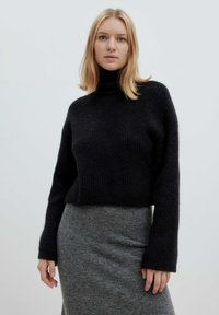 Zwarte gebreide turtleneck trui met lange mouwen, cropped ontwerp, textiele stof, gedragen met een grijze rok.