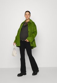 Casaco de lã verde oversized, blusa de rendas preta, calças pretas largas, botas pretas chunky e bolsa branca. Textura suave e design estruturado.