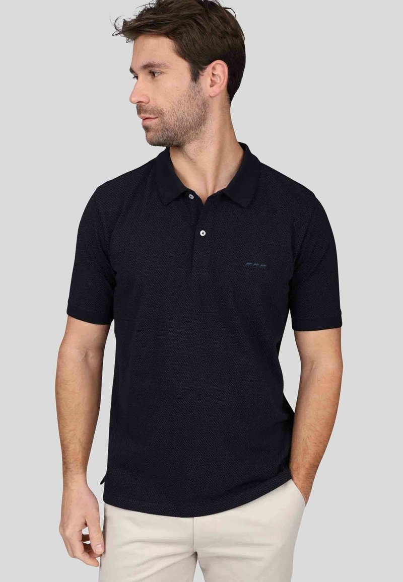 Polo shirt bleu marine foncé avec un motif texturé, manches courtes et un col contrasté. Détail de logo discret sur la poitrine. Design ajusté.