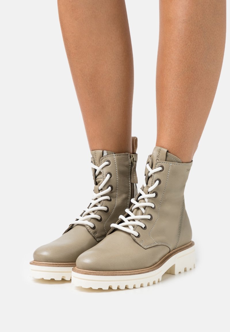 Bottes cheville en cuir gris clair avec lacets blancs, col rembourré et semelle blanche épaisse. Dotées d'une fermeture éclair latérale pour un enfilage facile.