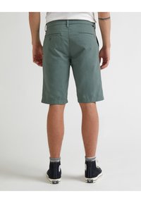 Zelené bavlněné šortky s volným střihem, které mají dvě zadní kapsy a ohrnutý lem, doplněné černými vysokými botami.