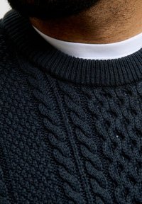 Navy knitted sweater with a textured cable pattern, featuring a ribbed crew neckline layered over a white shirt collar.
