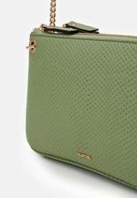 Borsa a tracolla in pelle verde texturizzata con cerniera dorata e tracolla a catena. Presenta un piccolo logo decorativo. Superficie liscia e a motivi.
