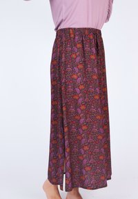 Langer, floraler Rock mit einer Farbpalette aus Lila und Braun, ergänzt durch rote, orange und grüne Akzente. Elastischer Taillenbund; leichtes Material.
