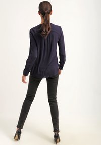 Blouse bleu marine à manches longues avec une texture lisse, associée à un jean noir ajusté. La tenue est complétée par des chaussures à talons hauts noires.