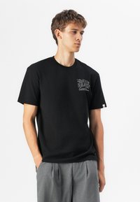 Black short-sleeve t-shirt made from cotton, featuring a logo print on the left chest and a small tag on the sleeve. Plain design.