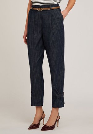 Hogewaisted, donkerblauwe gestreepte broek met plooien, zijzakken en een enkel lengte, gecombineerd met een bruine riem en bordeauxrode hoge hakken.
