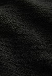 Čierny fleece materiál s textúrovaným, mäkkým povrchom. Tkanina pôsobí mäkko a ľahko, s jednotnou tmavou farbou po celom obvode.
