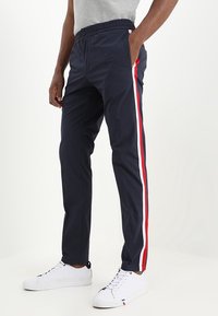 Navy sweatpants with a drawstring waist, side pockets, and contrasting red and white stripes along the outer seams. Cotton blend material.