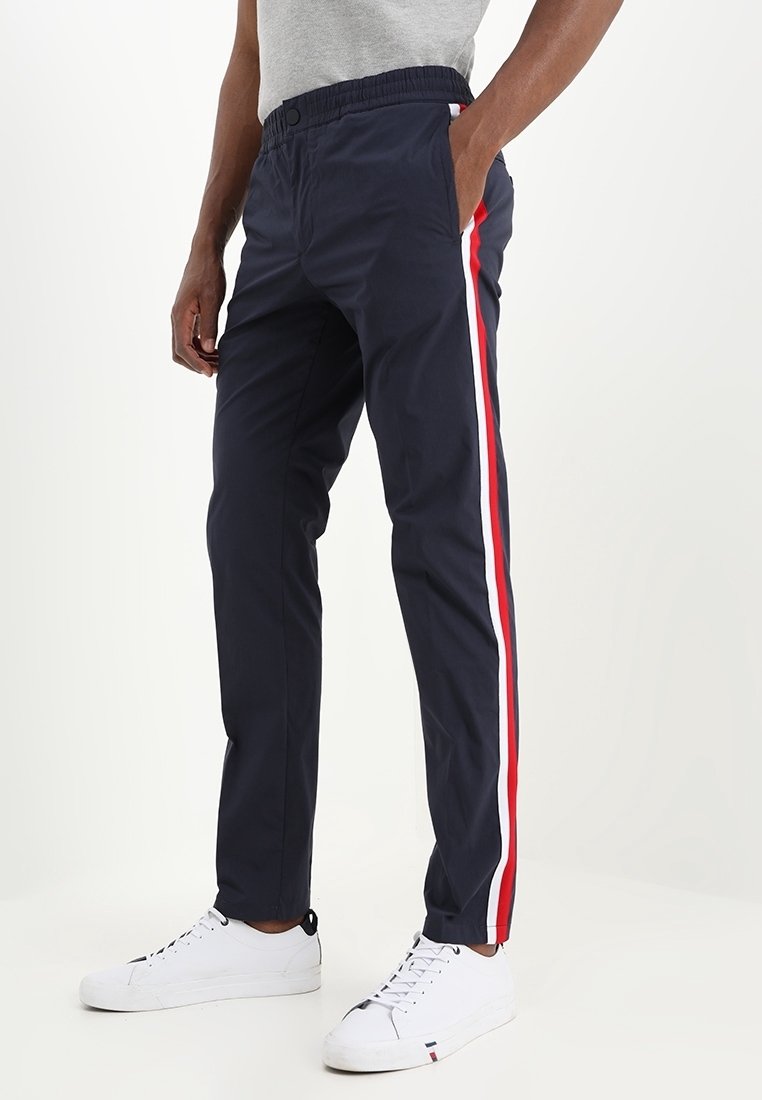 Marineblauwe sweatpants met een koord in de taille, zijzakken en contrasterende rode en witte strepen langs de buitennaden. Materiaal van katoenmix.