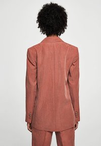 Blazer rosa con un design strutturato, tessuto texturizzato, rever affilati e accentuazioni a tre bottoni sui polsini, visto da dietro.