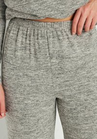Grijze gebreide loungebroek met een elastische tailleband. De stof heeft een gemêleerd textuur met verschillende tinten grijs. Geen zichtbare zakken.