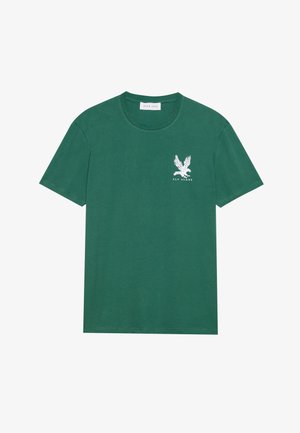 Green cotton t-shirt featuring a round neck, short sleeves, and a white eagle graphic with the text "FLY ALONE" on the left chest.