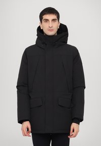 Jachetă izolată neagră cu glugă, având buzunare mari în față, croială dreptă și o textură netedă. Design minimalist.