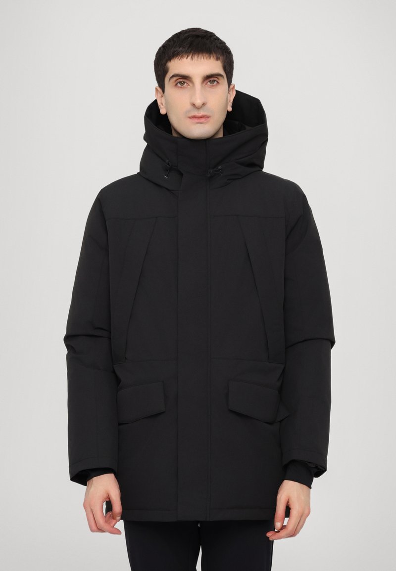 Jachetă izolată neagră cu glugă, având buzunare mari în față, croială dreptă și o textură netedă. Design minimalist.