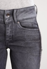 Jeans de mezclilla gris con una textura suave, que presentan una botonera y cremallera, bolsillos frontales y detalles de costura sutiles.