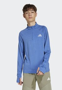 Modrá športová dlhá rukávová košeľa s štvrťovým zipsom, s textúrovanou látkou a malým bielym logom Adidas na ľavej hrudi.