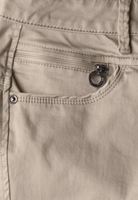 Pantalons en coton beige avec une poche frontale à fermeture éclair, quincaillerie en argent et détails de couture contrastants.