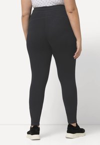 Schwarze Leggings mit einem hohen Bund, weicher Textur und enganliegendem Design. Der Stoff wirkt dehnbar und wird von dunklem Schuhwerk ergänzt.