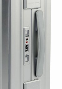 Maleta plateada con un acabado texturizado, que cuenta con un asa de cuero gris, cerradura de combinación y una ranura para llave TSA en el lateral.