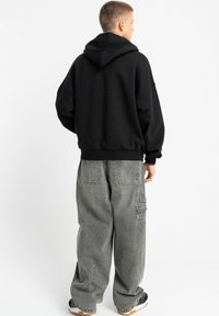 Czarna bluza z kapturem o dużej sylwetce, wykonana z miękkiego materiału, z prążkowymi mankietami, w zestawie z luźnymi szarymi spodniami typu cargo z wieloma kieszeniami.