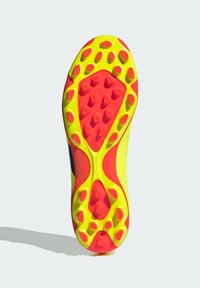 Suela de una zapatilla deportiva con goma de color amarillo brillante y rojo, con textura antideslizante, picos redondeados para tracción y un diseño aerodinámico.