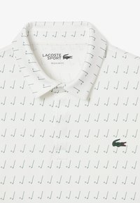 Polo bianco con vestibilità regolare, stampato con motivi di note musicali verdi. Include il logo del coccodrillo verde Lacoste sul petto.