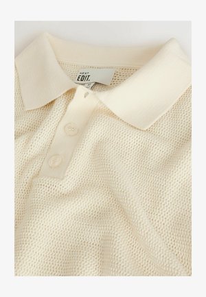Polo shirt couleur crème avec un tricot texturé, doté d'un col classique et d'une patte de boutonnage à trois boutons. Étiquette de marque visible à l'intérieur du col.