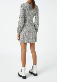 Vestido floral en blanco y negro con mangas largas, cintura fruncida y falda acampanada. Combinado con botas de combate blancas con cordones.