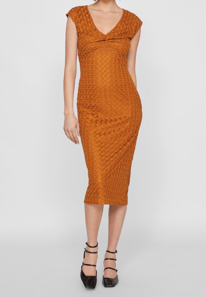 Braunes, angepasstes Midikleid mit einem strukturierten, geometrischen Muster, kurzen Ärmeln und einem V-Ausschnitt. Kombiniert mit schwarzen Riemchenheels.