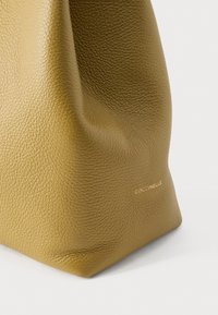 Kožená taška olivově zelené barvy s texturovaným povrchem, měkkým látkovým designem a minimálním značením zlatým písmem blízko základny.