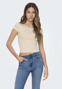 Lys beige tettsittende ribbestrikket topp med korte ermer, kombinert med lyseblå høytlivsjeans, som viser et avslappet og moderne utseende.
